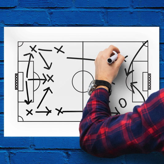 Person drawing a soccer strategy diagram on a whiteboard against a blue brick wall