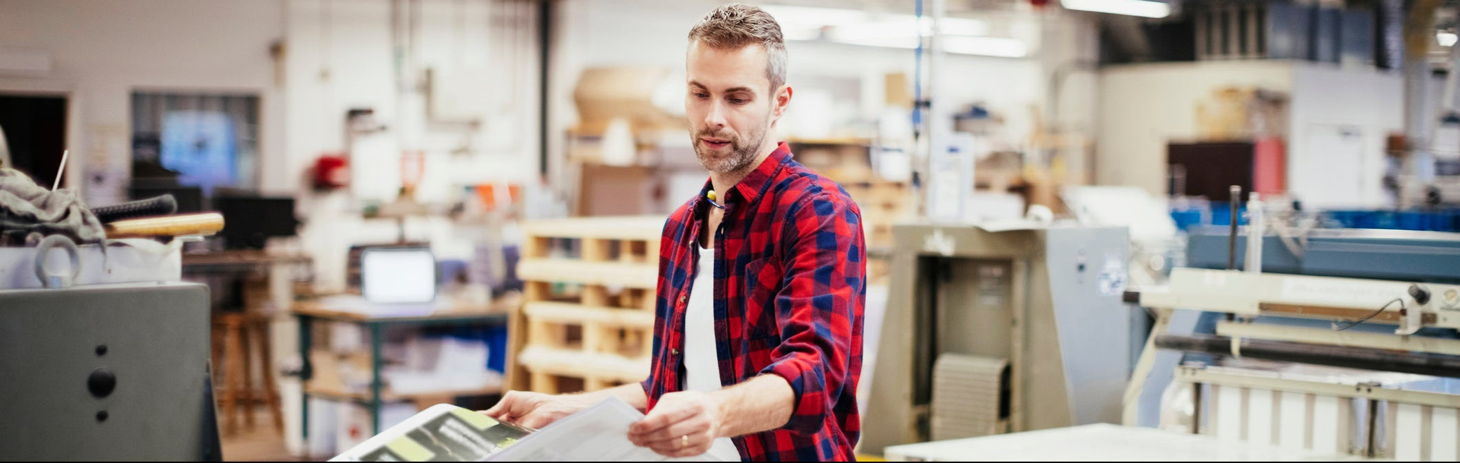 Man in a red plaid shirt working with paper in a print room setting